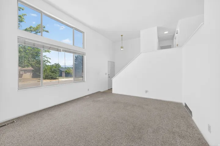 Living space featuring a large picture window with transom, neutral carpet, white walls, and a staircase leading to an upper level