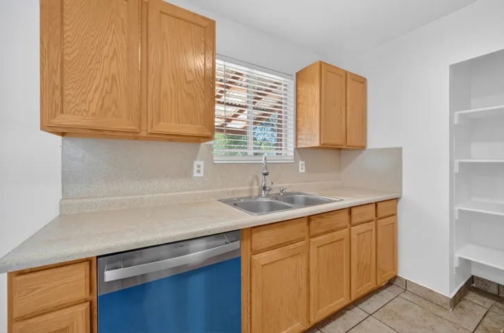 Kitchen featuring ample light wood cabinetry, a double basin stainless steel sink, light-toned countertop with integrated backsplash, and a stainless steel dishwasher