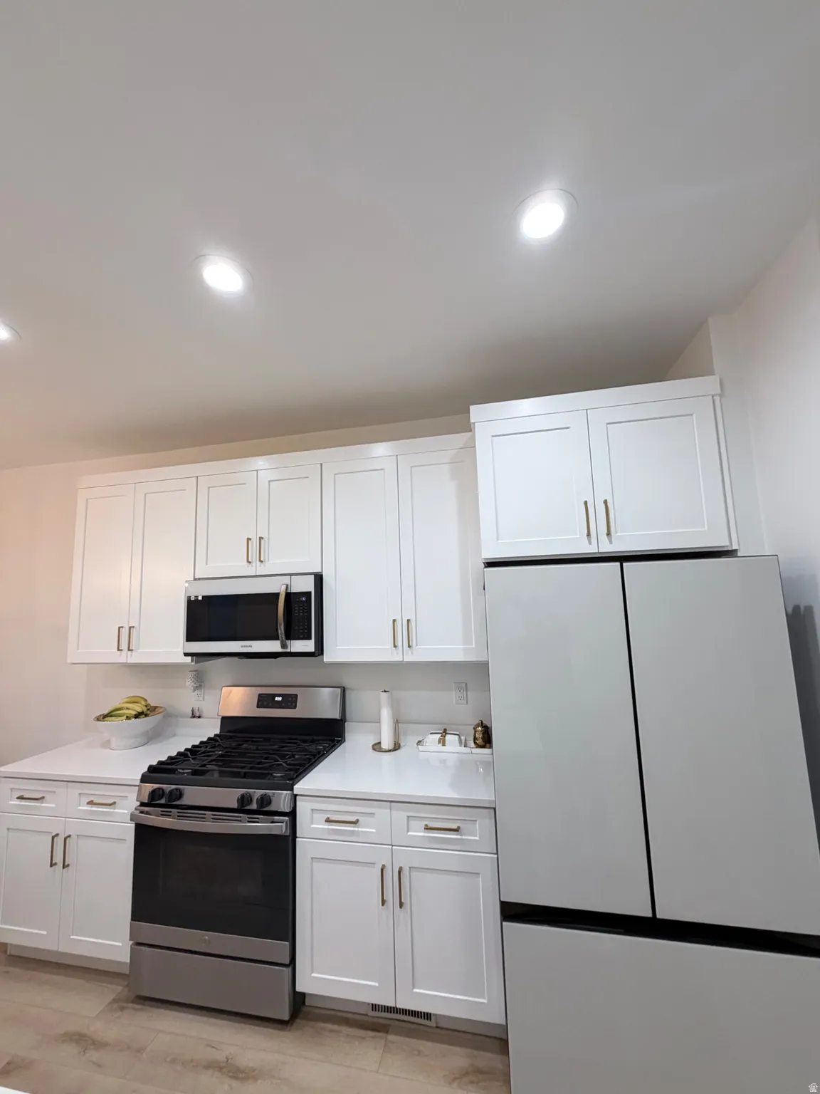 Modern kitchen featuring white shaker cabinetry, stainless steel appliances, light-toned countertops, and recessed ceiling lighting
