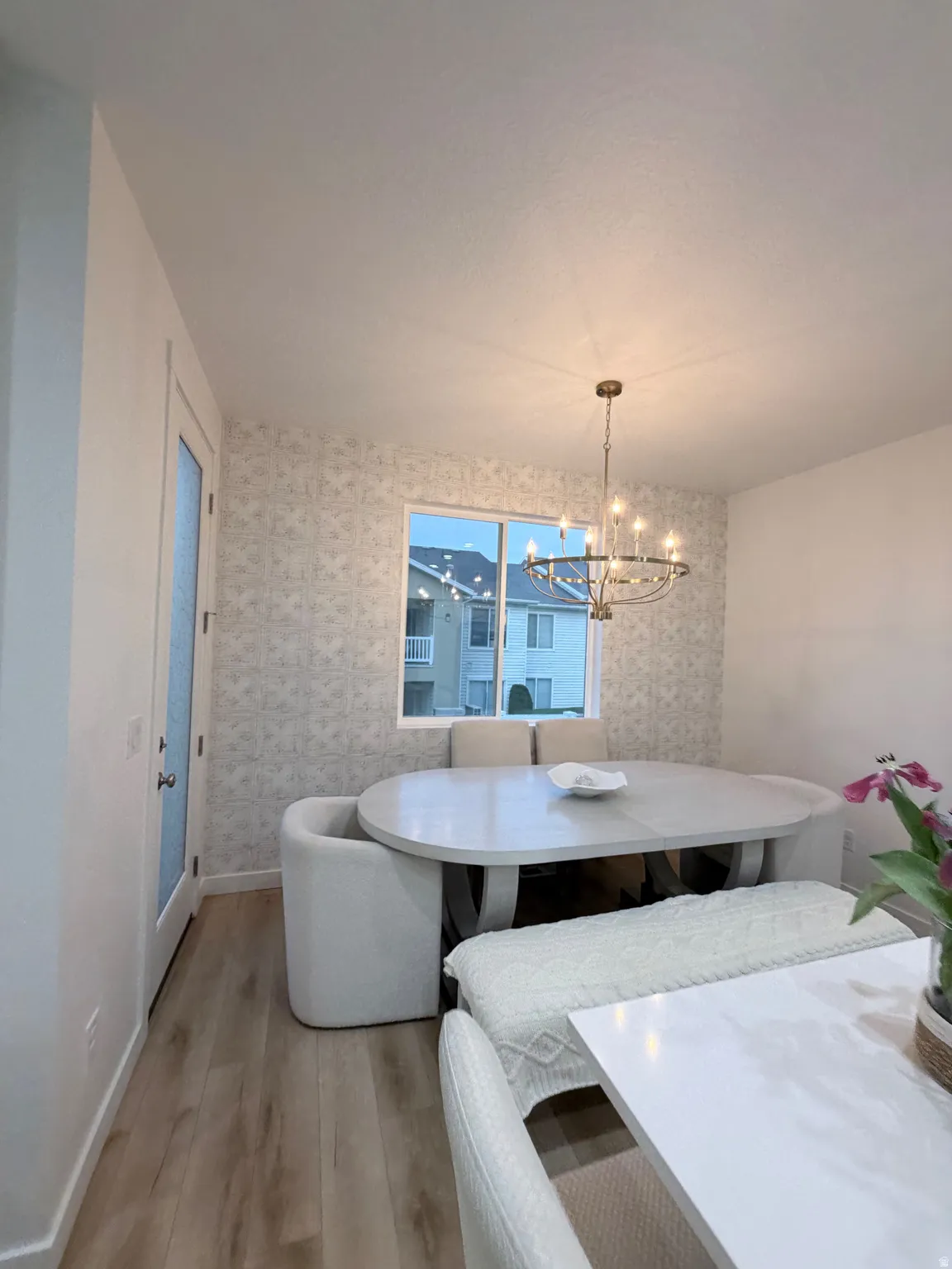 Dining area featuring wood-finish flooring, a contemporary chandelier, and an accent wall with patterned wallpaper