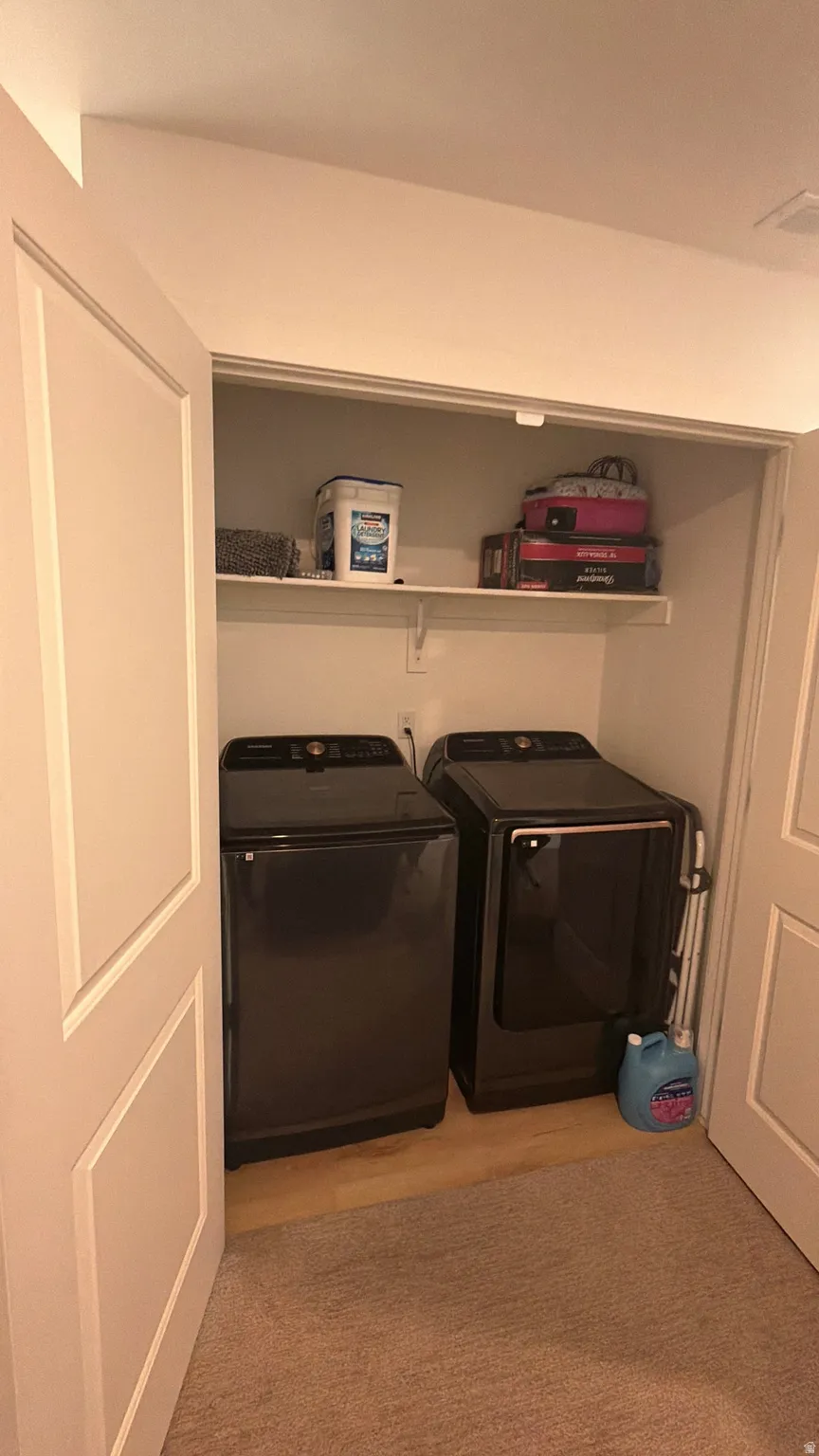 Dedicated laundry closet featuring a washer and dryer, built-in shelving, and wood-finish flooring