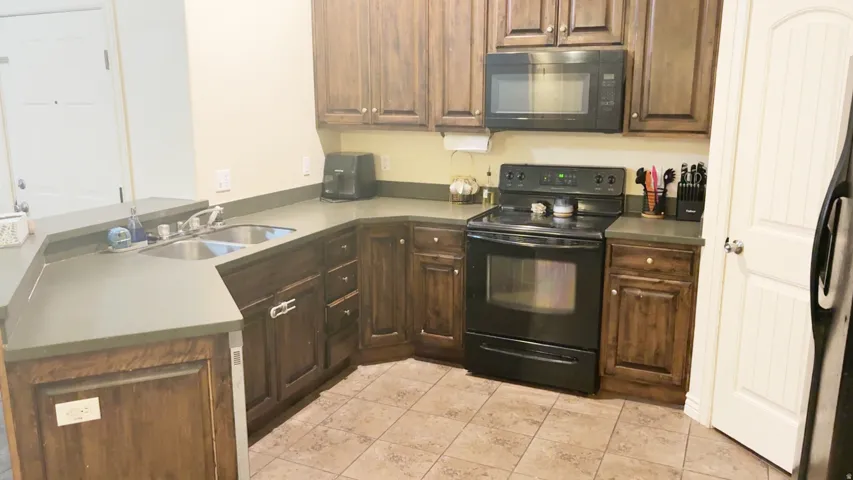 Kitchen featuring dark wood cabinetry, solid surface countertops, a double basin stainless steel sink, black electric range, and a built-in microwave