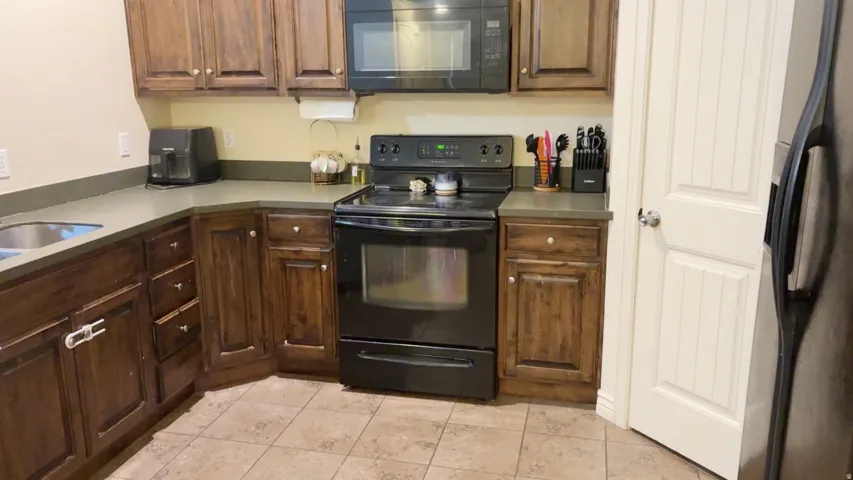 Kitchen featuring dark wood cabinetry, a black electric range, a black built-in microwave, and a stainless steel sink