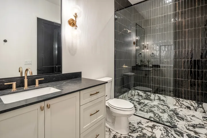 Bathroom featuring a white vanity with gold-tone hardware, a dark countertop, and a rectangular undermount sink with a gold-tone faucet
