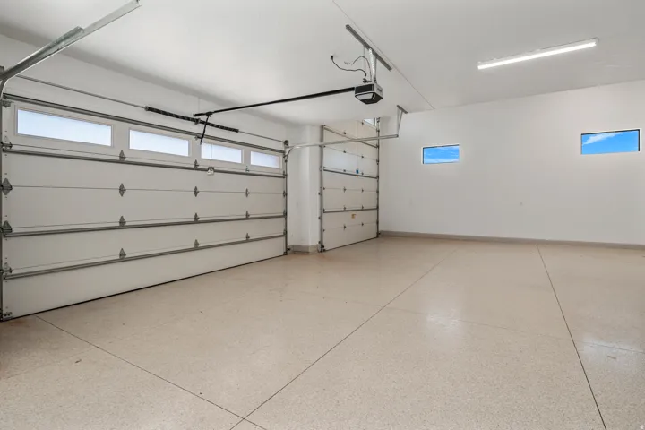 Two-car garage featuring two white panel overhead doors with upper window inserts, an epoxy-coated concrete floor, and two high horizontal windows