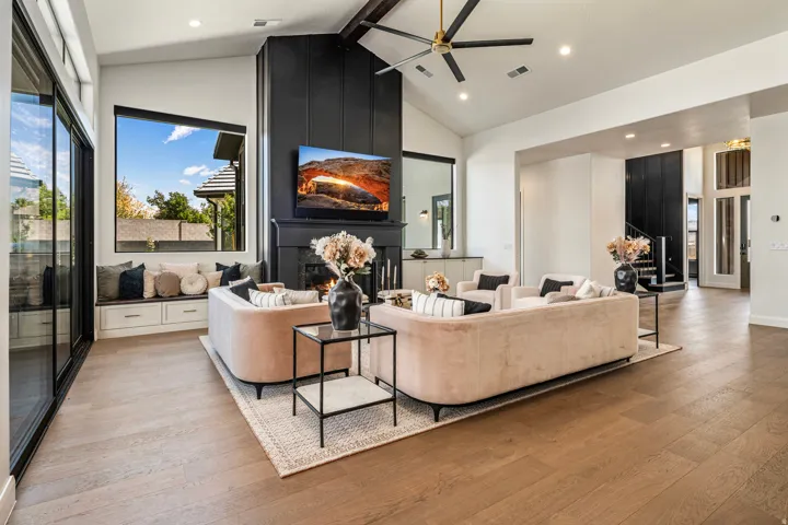 Expansive living space featuring vaulted ceilings, wood-finish flooring, a contemporary fireplace with a dark paneled surround, a built-in window seat with storage, and large sliding glass doors