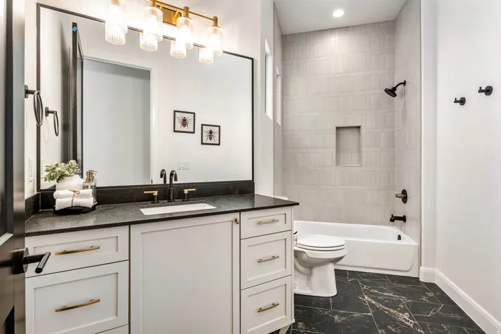 Contemporary bathroom with a dark-framed mirror, white vanity with gold-tone hardware, black countertop, and a white undermount sink with a matte black and gold-tone faucet