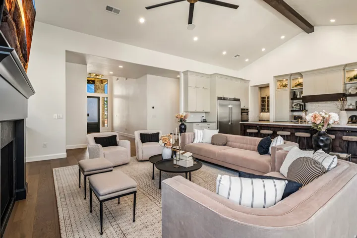 Open-concept living space featuring wood-finish flooring, a fireplace with a dark mantel, a high vaulted ceiling with exposed beams, recessed lighting, and a ceiling fan