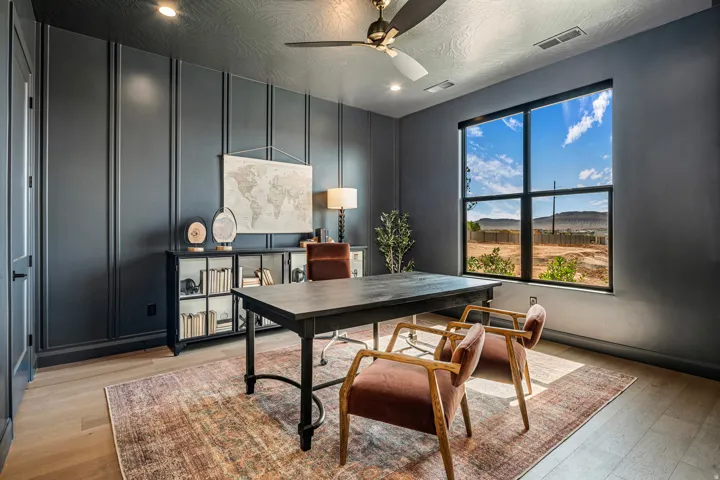 Office space featuring dark paneled walls, light wood-finish flooring, and a large window with a desert landscape