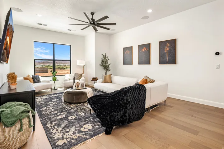 Spacious living area featuring light wood-finish flooring, a large black-framed window, a contemporary ceiling fan, recessed lighting, and integrated ceiling speakers