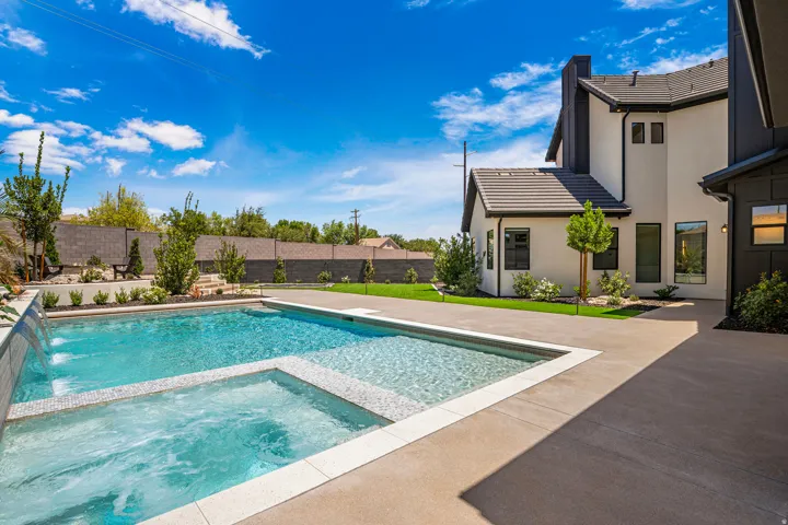 Contemporary stucco home featuring a dark tile roof, a large swimming pool with integrated spa, a water feature, and a spacious concrete patio