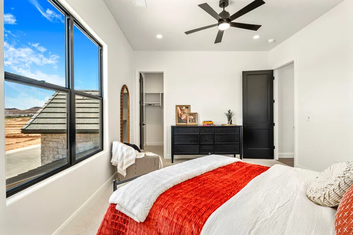 Spacious bedroom featuring large black-framed windows, a black ceiling fan with integrated lighting, and a built-in closet with shelving