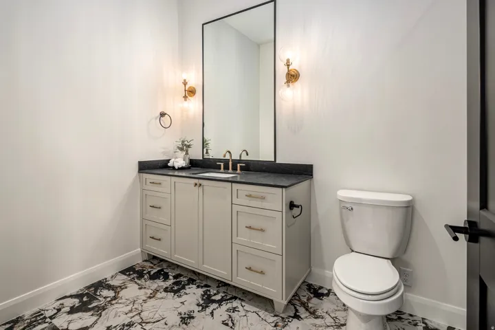Powder room featuring a single vanity with a dark countertop and gold-toned hardware, a rectangular mirror with a black frame, and two wall sconces