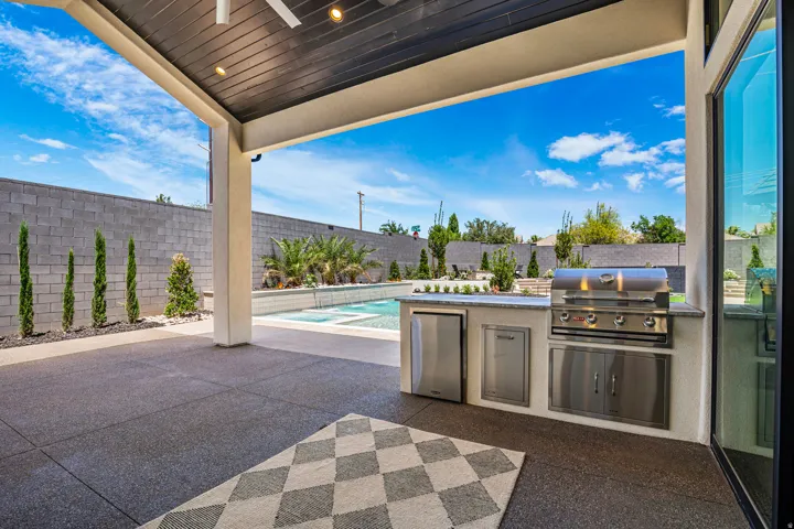 Covered patio with integrated outdoor kitchen featuring a built-in grill and stainless steel appliances
