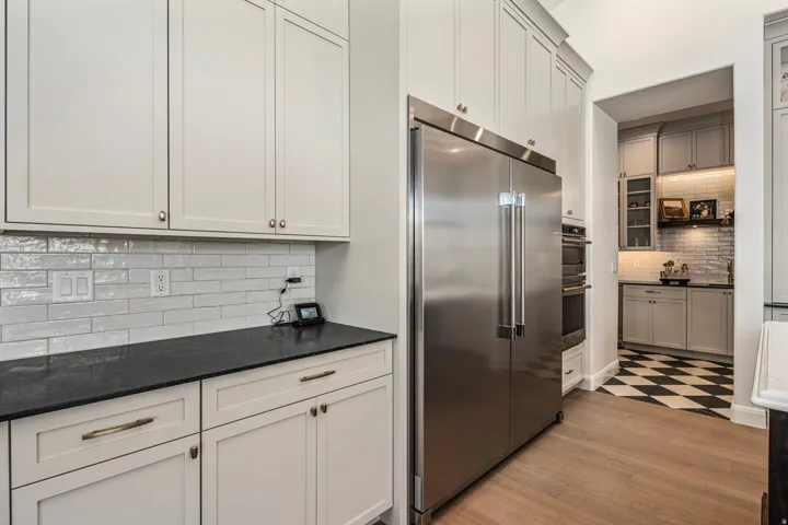 Gourmet kitchen featuring a stainless steel side-by-side refrigerator, double wall ovens, wood-finish flooring, and white shaker cabinetry with dark countertops