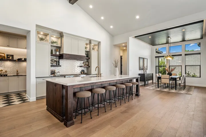 Open-concept kitchen and dining area featuring light wood-finish flooring, a substantial kitchen island with a light-toned countertop, and perimeter cabinetry with open shelving