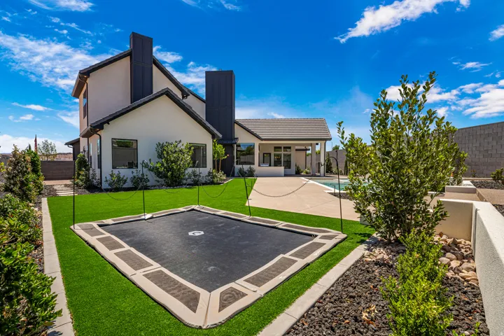 Expansive backyard featuring artificial turf, an in-ground trampoline, mature landscaping with decorative rock, concrete patio, and a swimming pool