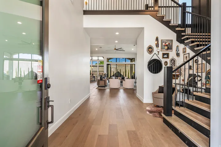 Grand entryway featuring wood-finish flooring, a contemporary staircase with black risers and metal balusters, and a double-height ceiling