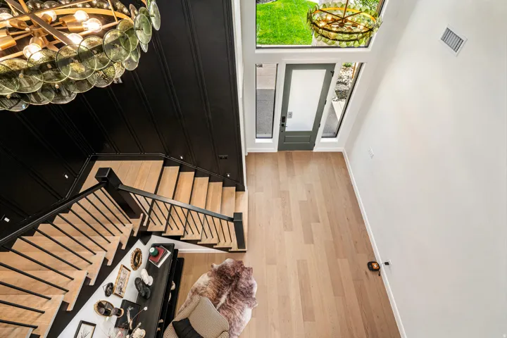 Two-story foyer featuring light wood-finish flooring, a grand staircase with black railings, and a prominent glass-disc chandelier