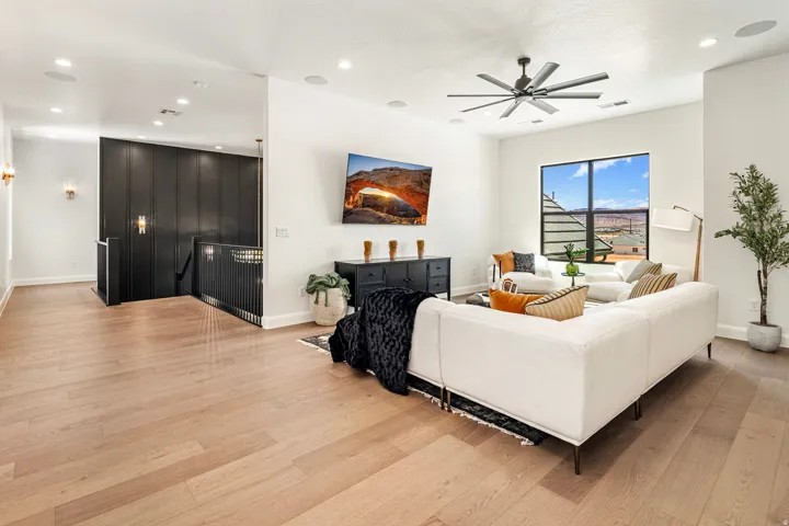 Spacious open-concept living area featuring light wood-finish flooring, a contemporary ceiling fan, recessed lighting, and a large window