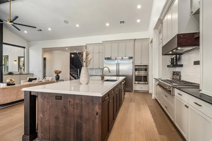 Spacious kitchen featuring a large island with a light-toned countertop, stainless steel appliances, wood-finish flooring, recessed lighting, and an open concept layout with a living area