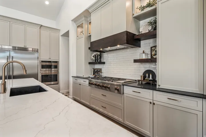 Gourmet kitchen featuring a large island with an undermount sink, built-in stainless steel appliances, a professional-grade range with a wood-accented hood, shaker-style cabinetry, and a white subway tile backsplash