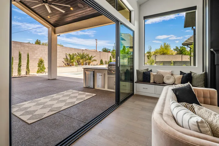 Expansive outdoor living area featuring a built-in outdoor kitchen with grill and refrigerator, a covered patio with a ceiling fan, and large format sliding glass doors