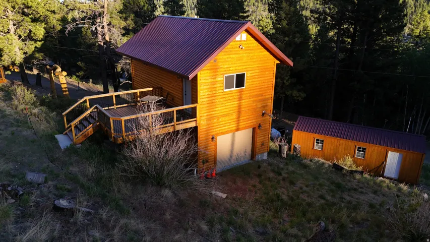 Wood-sided structure with a red corrugated metal roof, featuring a multi-level wood deck, an integrated garage, and a separate detached shed