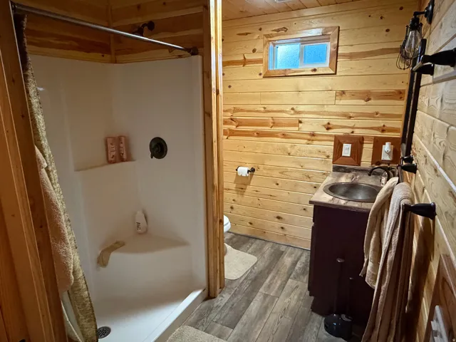 Bathroom featuring a corner shower, wood-finish flooring, wood plank walls, and a vanity with an integrated sink