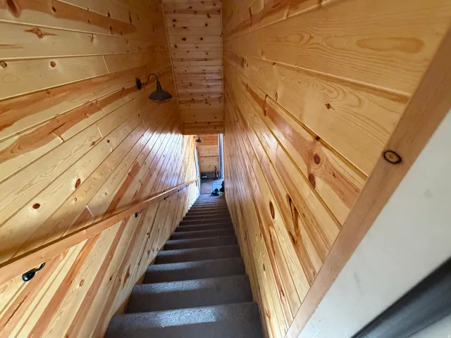 Carpeted staircase with light wood-paneled walls and ceiling