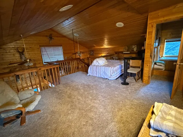 Spacious loft area featuring wood-paneled walls and ceiling, a substantial railing system, and neutral-toned carpeting