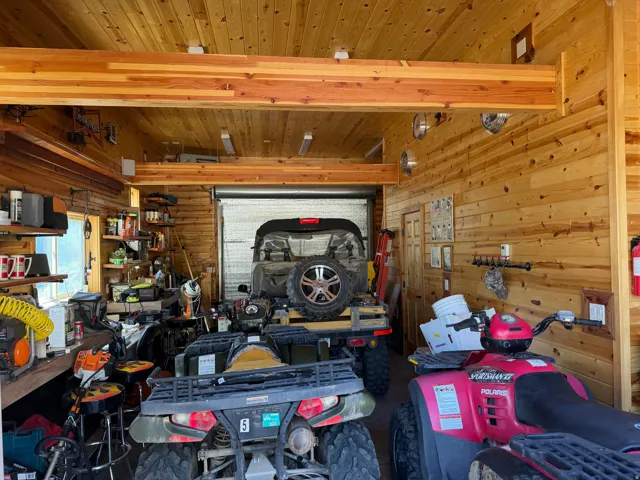 Spacious garage featuring light wood-finish plank walls and ceiling, exposed wood beams, and a roll-up garage door