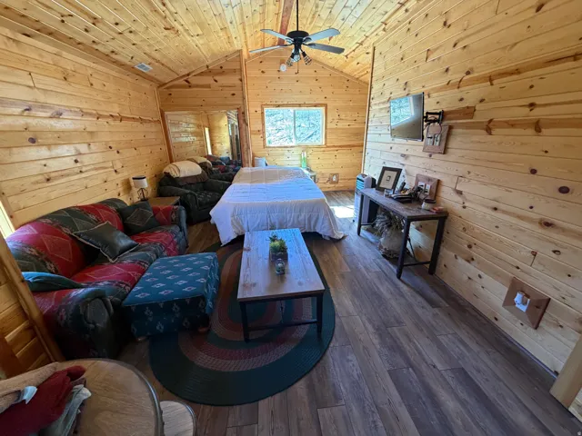 Vaulted ceiling interior featuring natural wood paneling throughout, wood-finish flooring, and a ceiling fan with integrated lighting