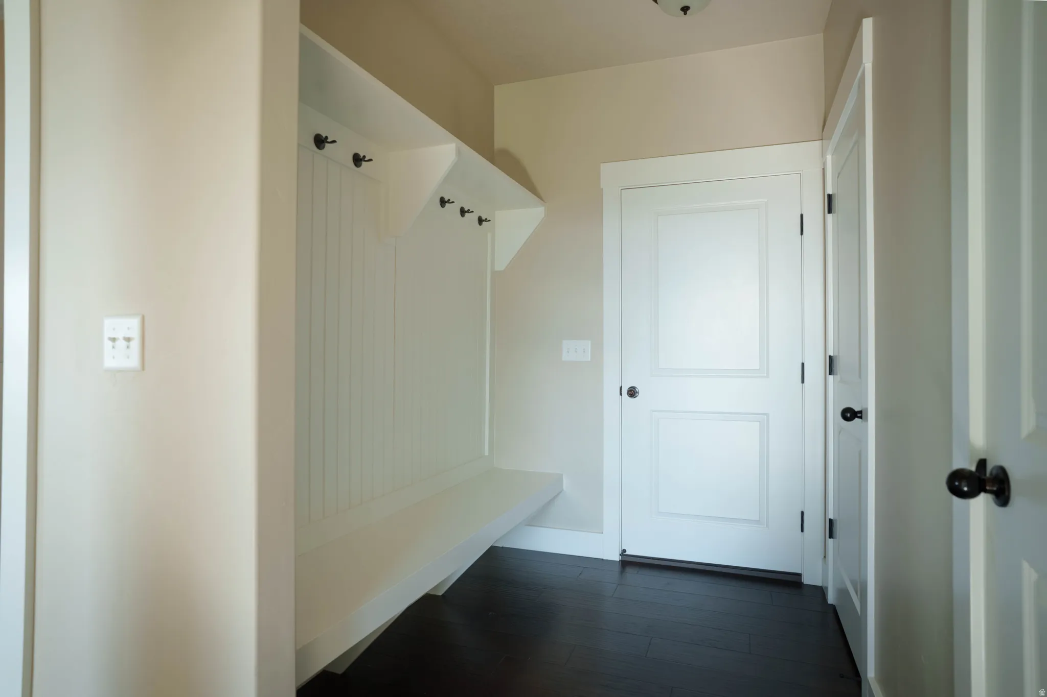 Entryway featuring dark wood-finish flooring, light-toned wall paint, and a built-in white bench with beadboard paneling and integrated hooks