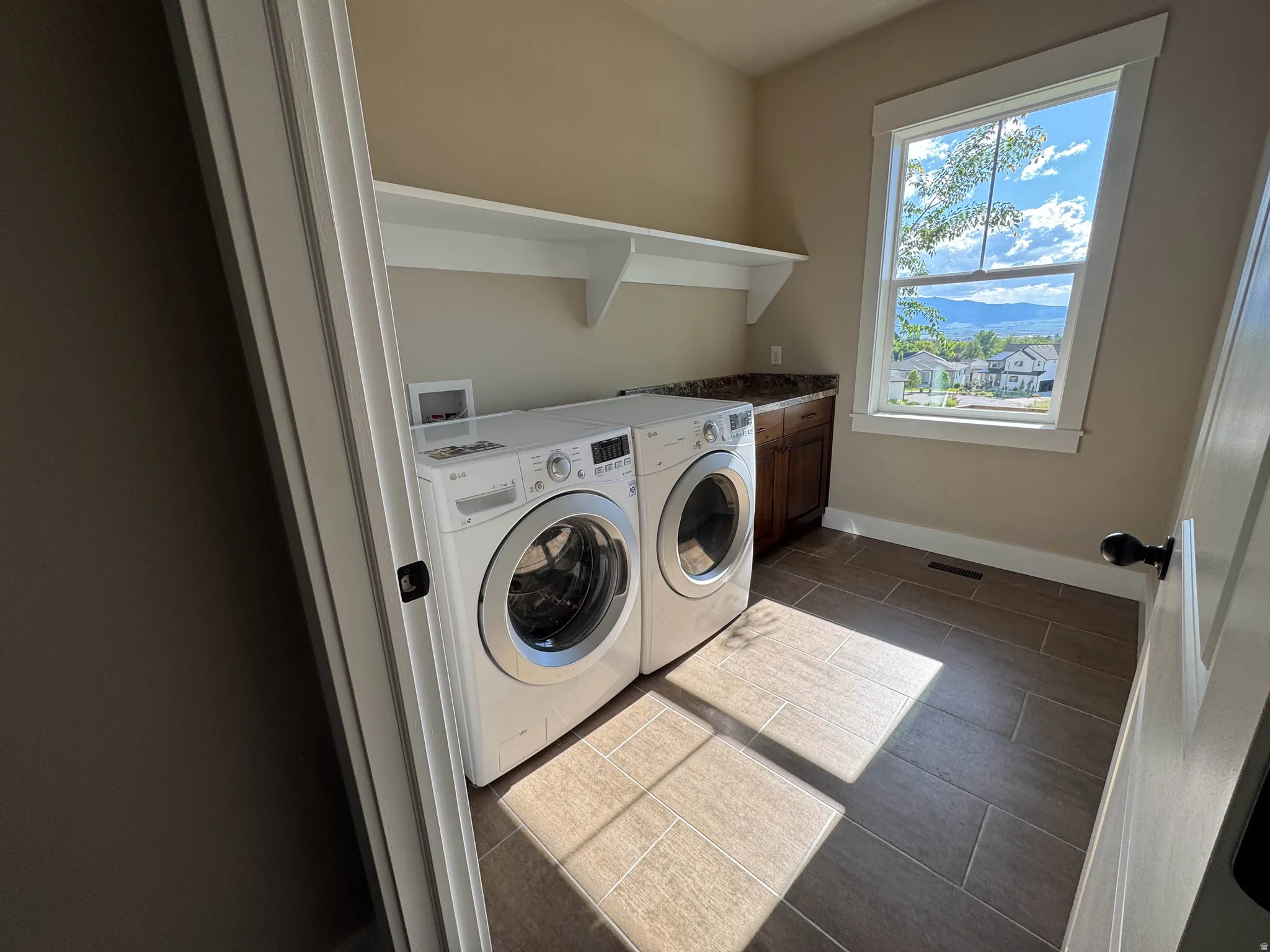Laundry area featuring a large window, built-in shelving, wood-finish cabinetry, a stone-look countertop, and wood-look tile flooring