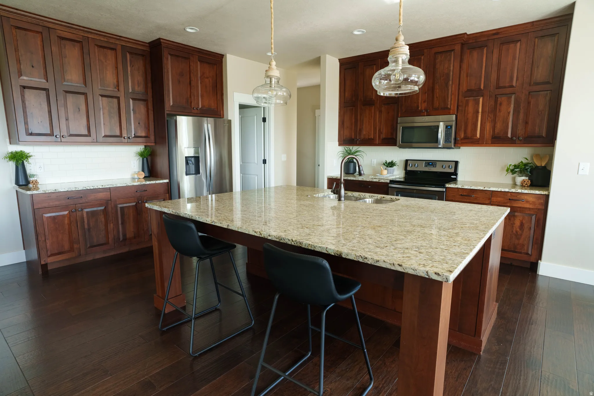 Kitchen featuring wood-finish flooring, a large island with a light-toned countertop, dark wood cabinetry, a stainless steel refrigerator, and a tile backsplash
