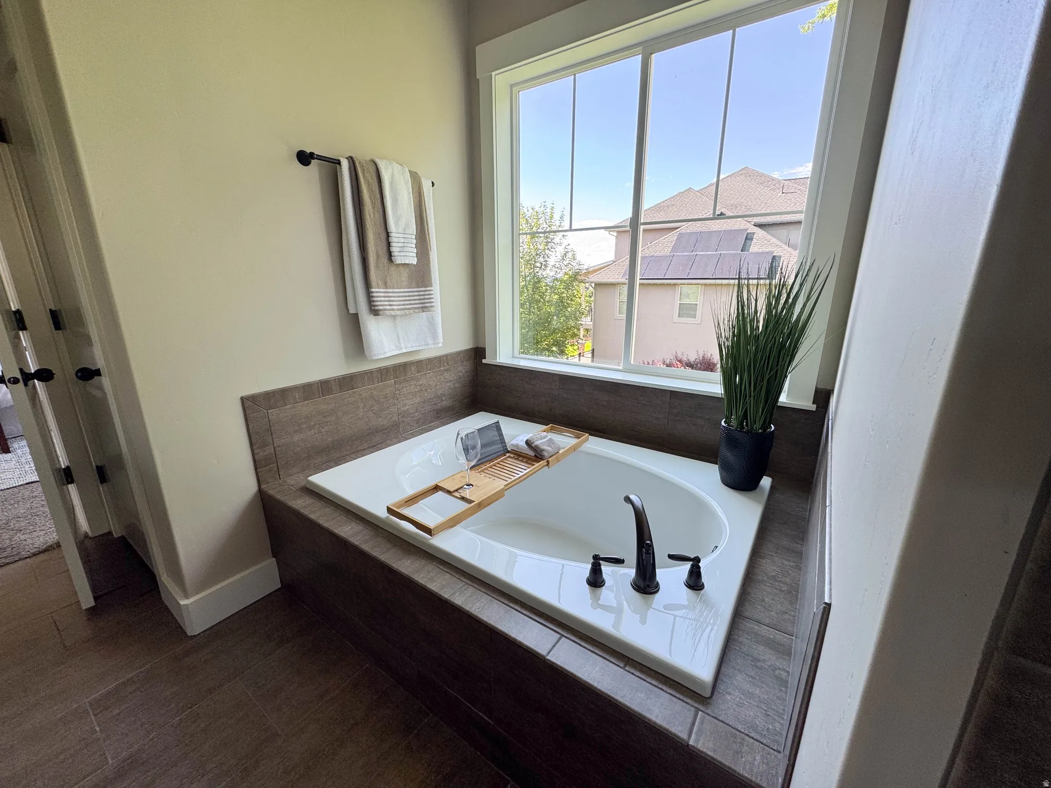 Built-in soaking tub with a dark bronze faucet, surrounded by wood-finish tile and a large window