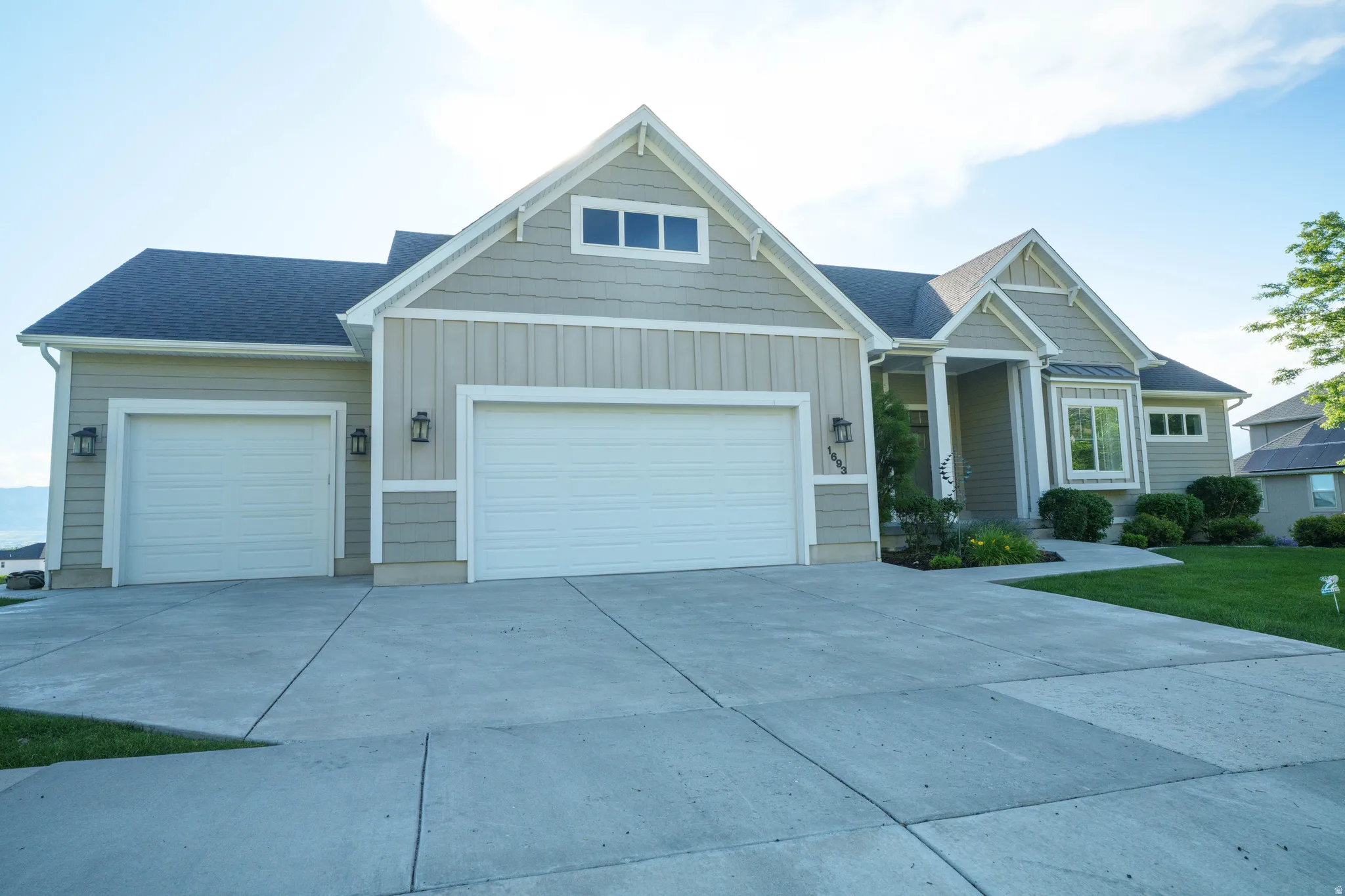Contemporary ranch-style exterior with a two-car garage, light tan siding, a dark roof, a bay window, and a concrete driveway