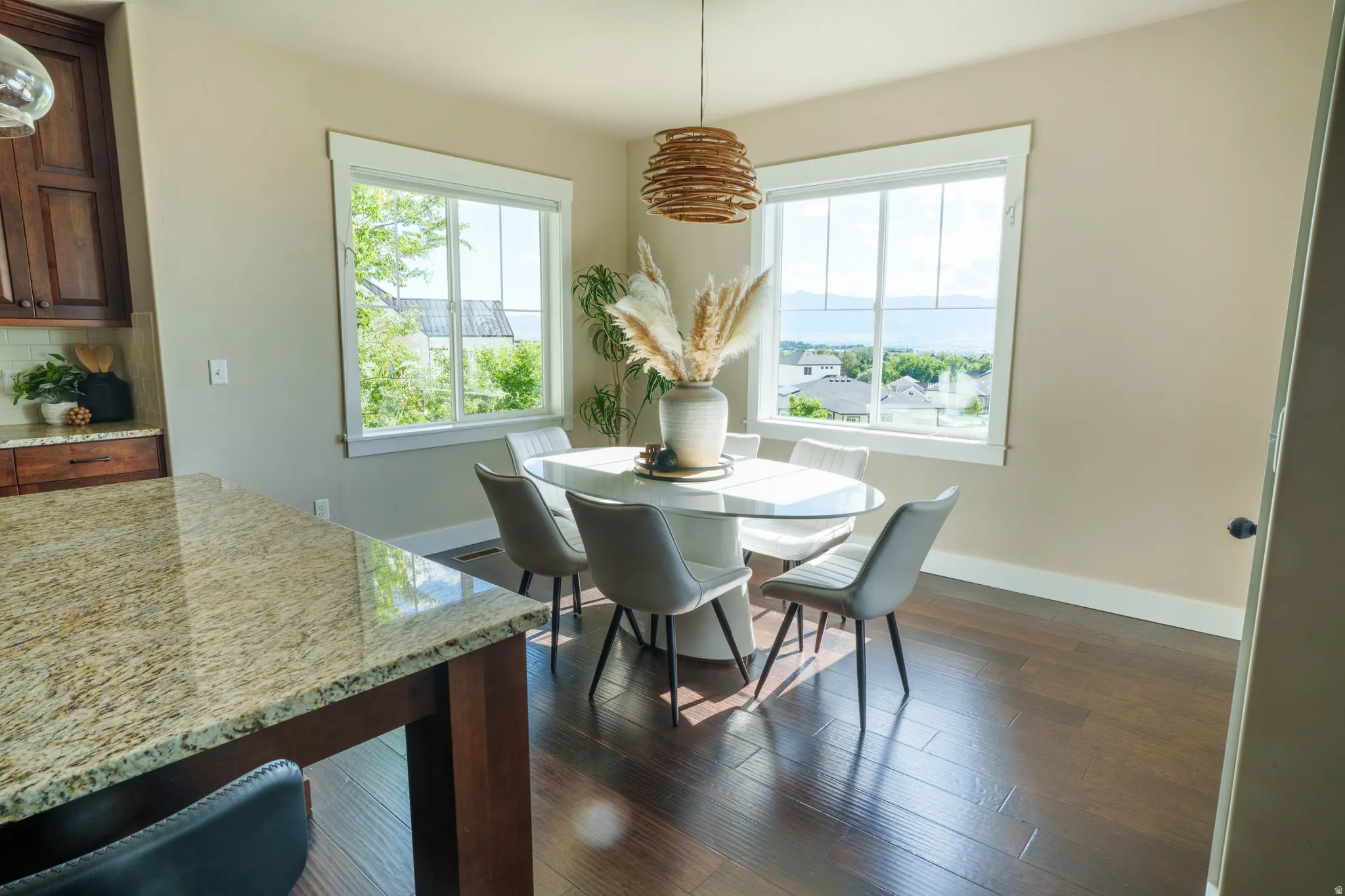 Open-concept dining area featuring dark wood-finish flooring, multiple large windows, and a woven pendant light fixture
