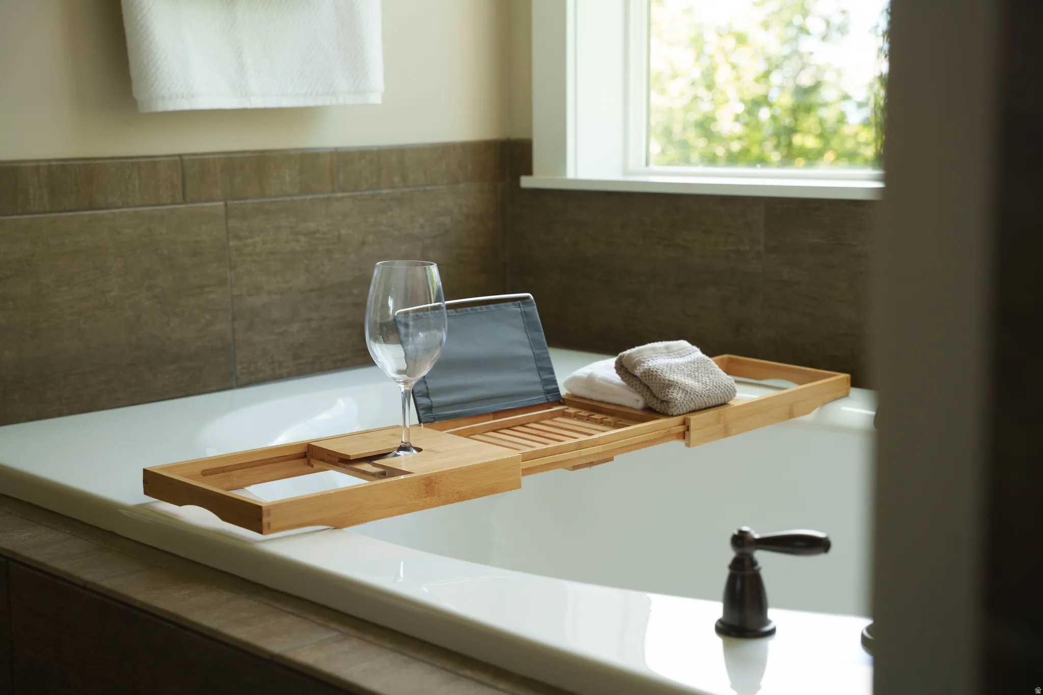 Soaking tub featuring a bronze-finish faucet, rectangular window, and floor-to-ceiling tile surround