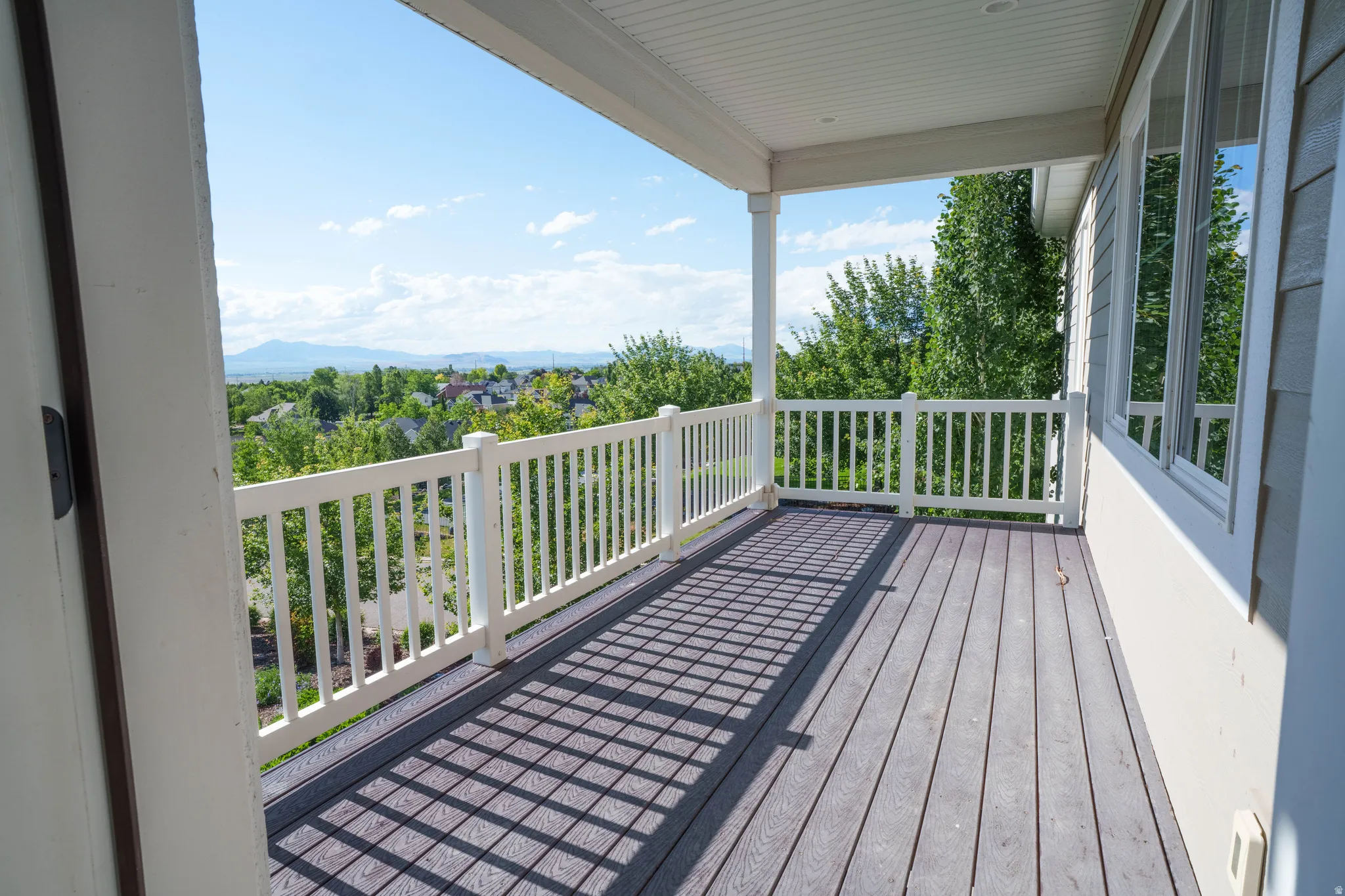 Spacious covered balcony featuring wood-finish decking, white baluster railing, and a serene landscape backdrop