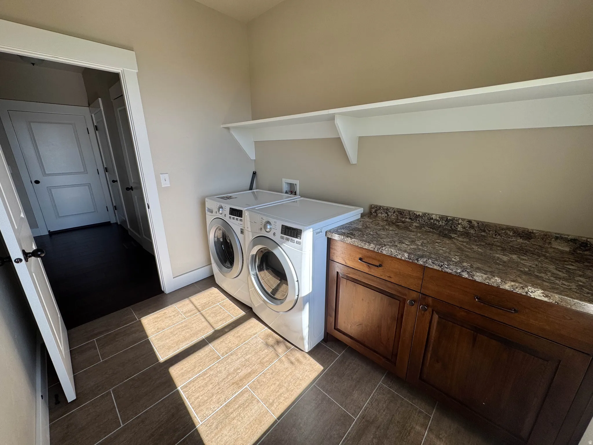 Laundry area featuring wood-finish tile flooring, built-in cabinetry with a patterned countertop, and an overhead shelving unit
