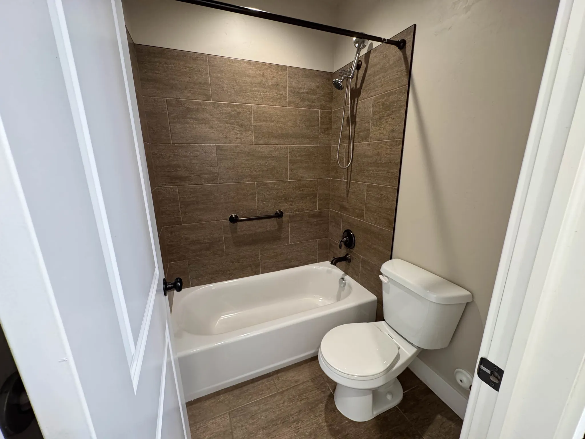 Full bathroom featuring a tub/shower combination with brown subway tile surround, matte black fixtures, and a coordinating grab bar