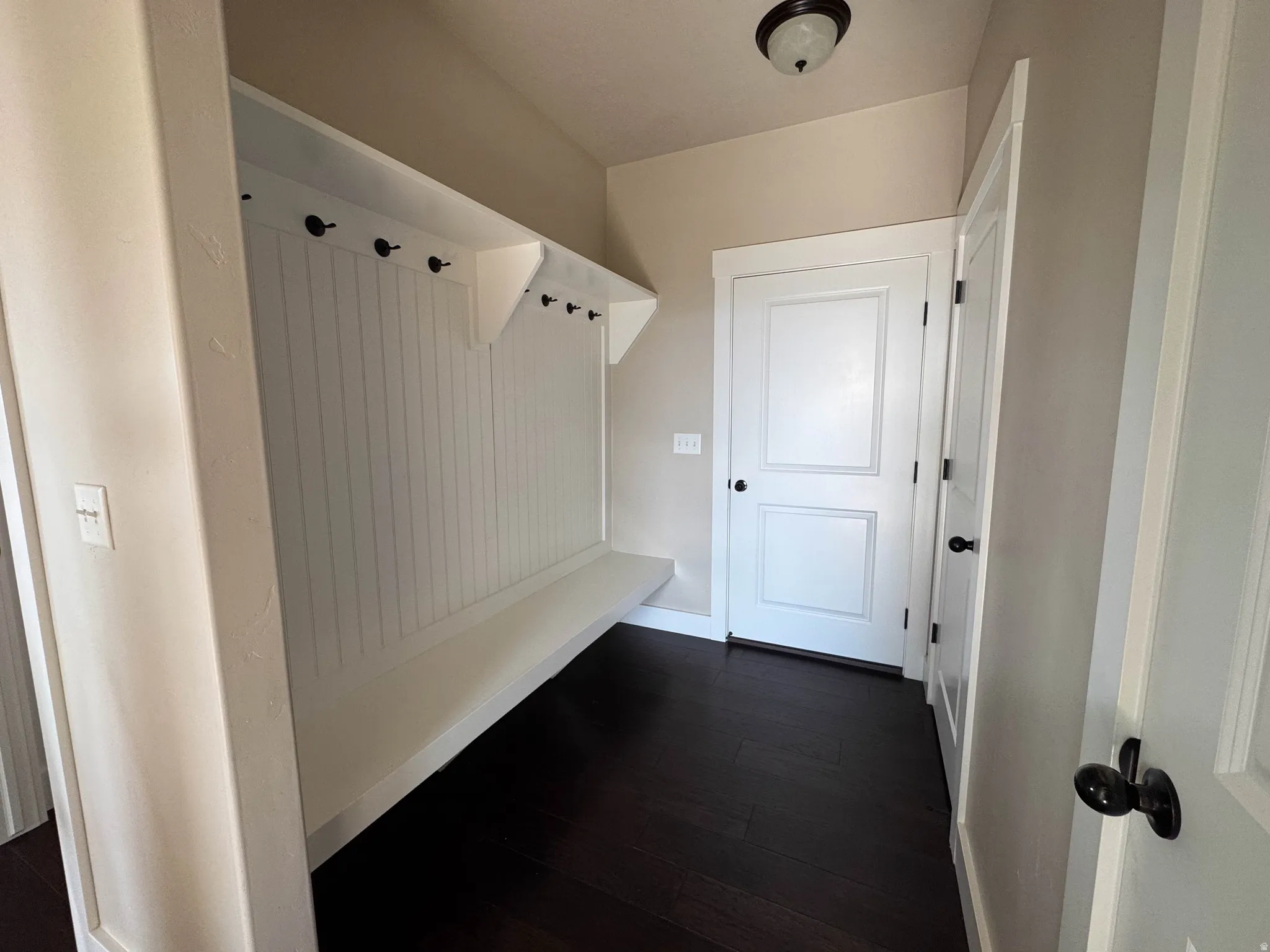 Entryway mudroom featuring a built-in bench, beadboard wainscoting, integrated coat hooks, dark wood-finish flooring, and panel doors with dark hardware