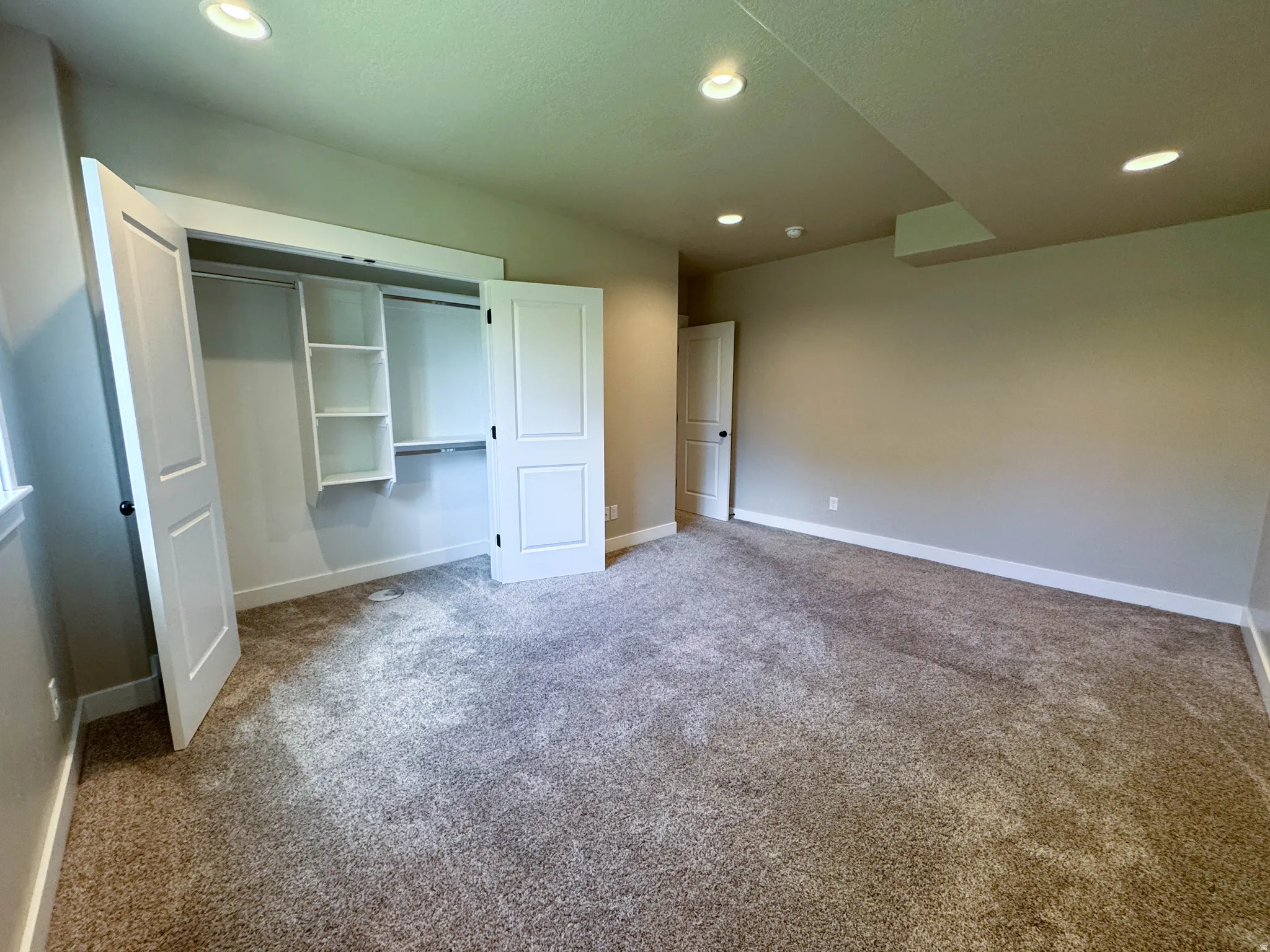 Spacious room featuring neutral carpet, recessed lighting, white baseboards, and a closet with bifold doors and built-in shelving