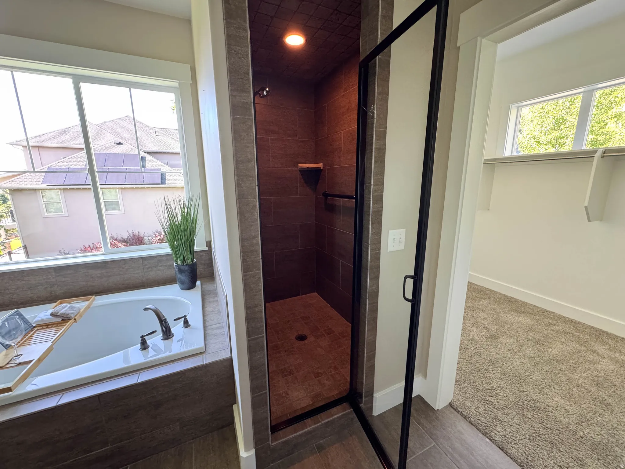 Walk-in shower with dark tile surround and built-in shelving, glass shower door with matte black framing, and a deep soaking tub with tile surround