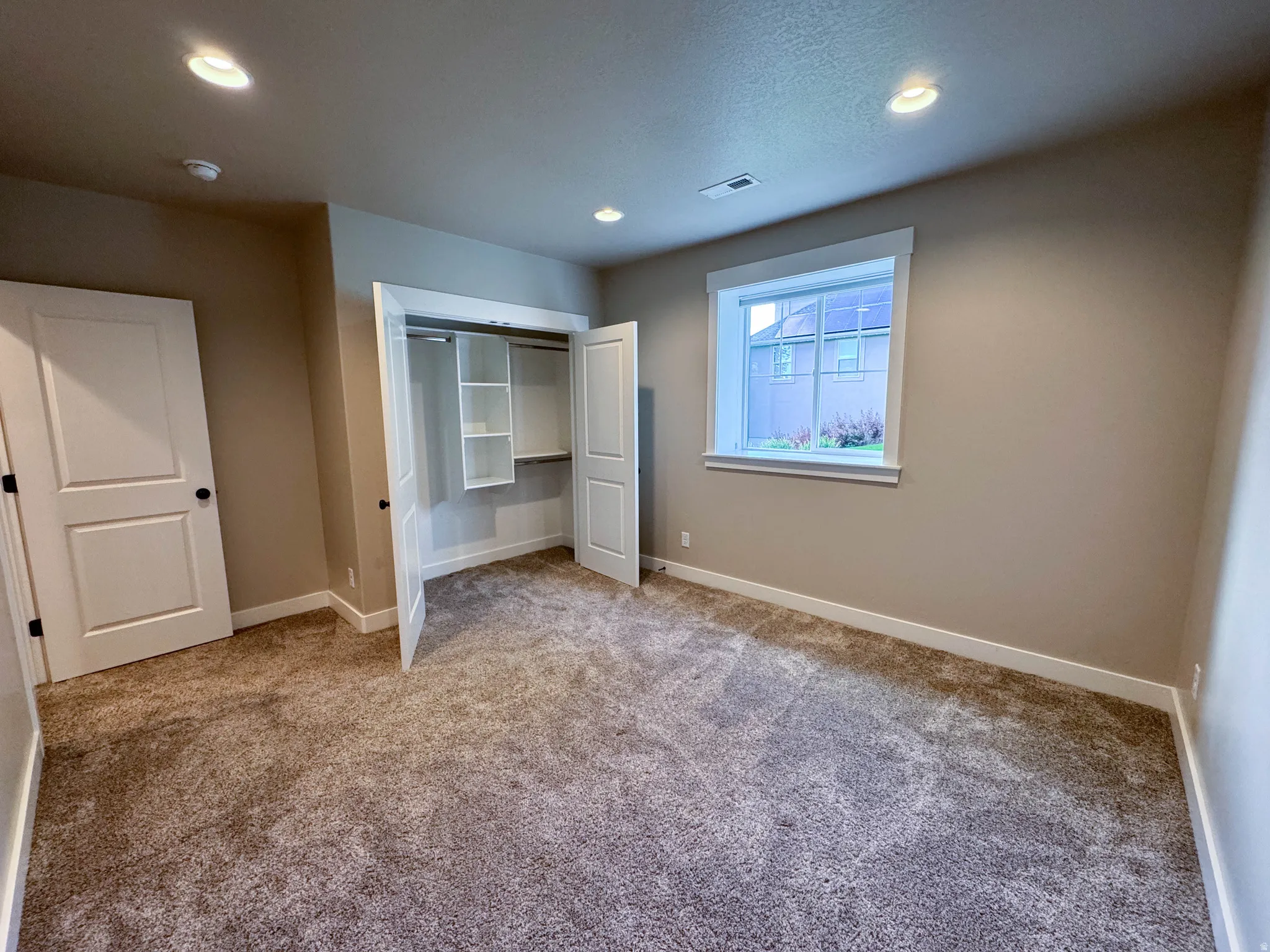 Carpeted room featuring a double-door closet with built-in shelving, recessed lighting, and a single window with white trim