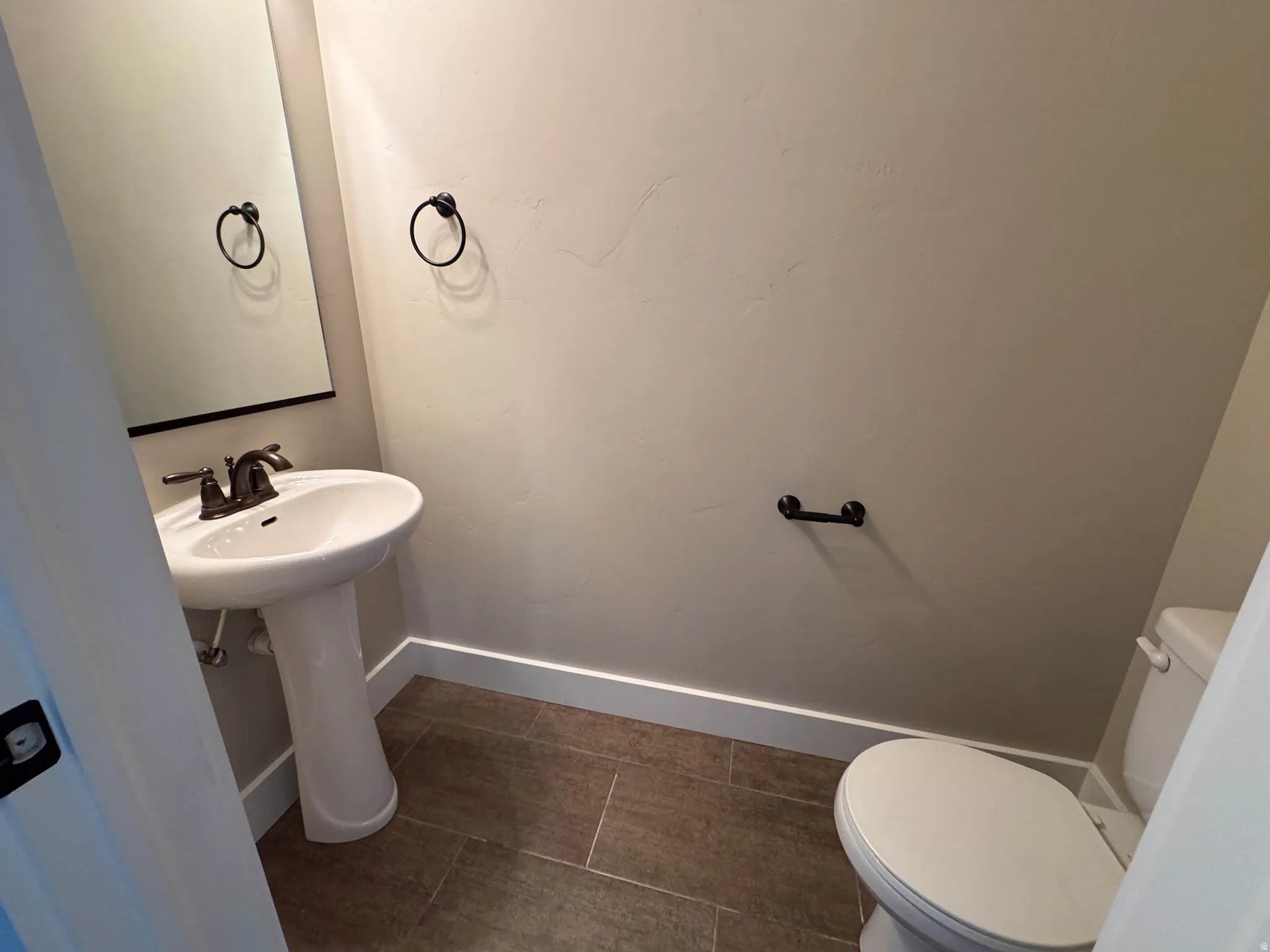 Pedestal sink with dark bronze fixtures, framed mirror, and tile flooring