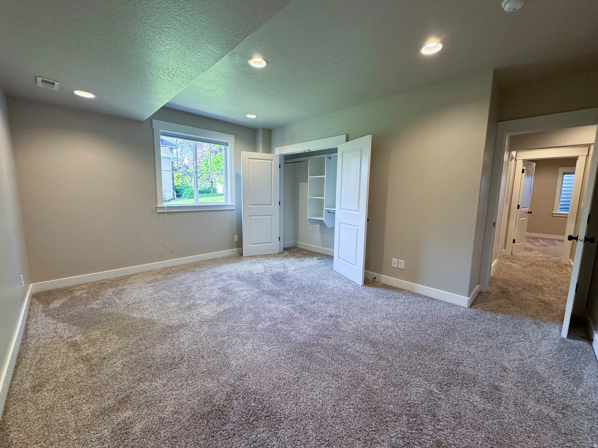 Carpeted room featuring a window with white trim, a double-door closet with shelving, recessed lighting, and a neutral paint palette