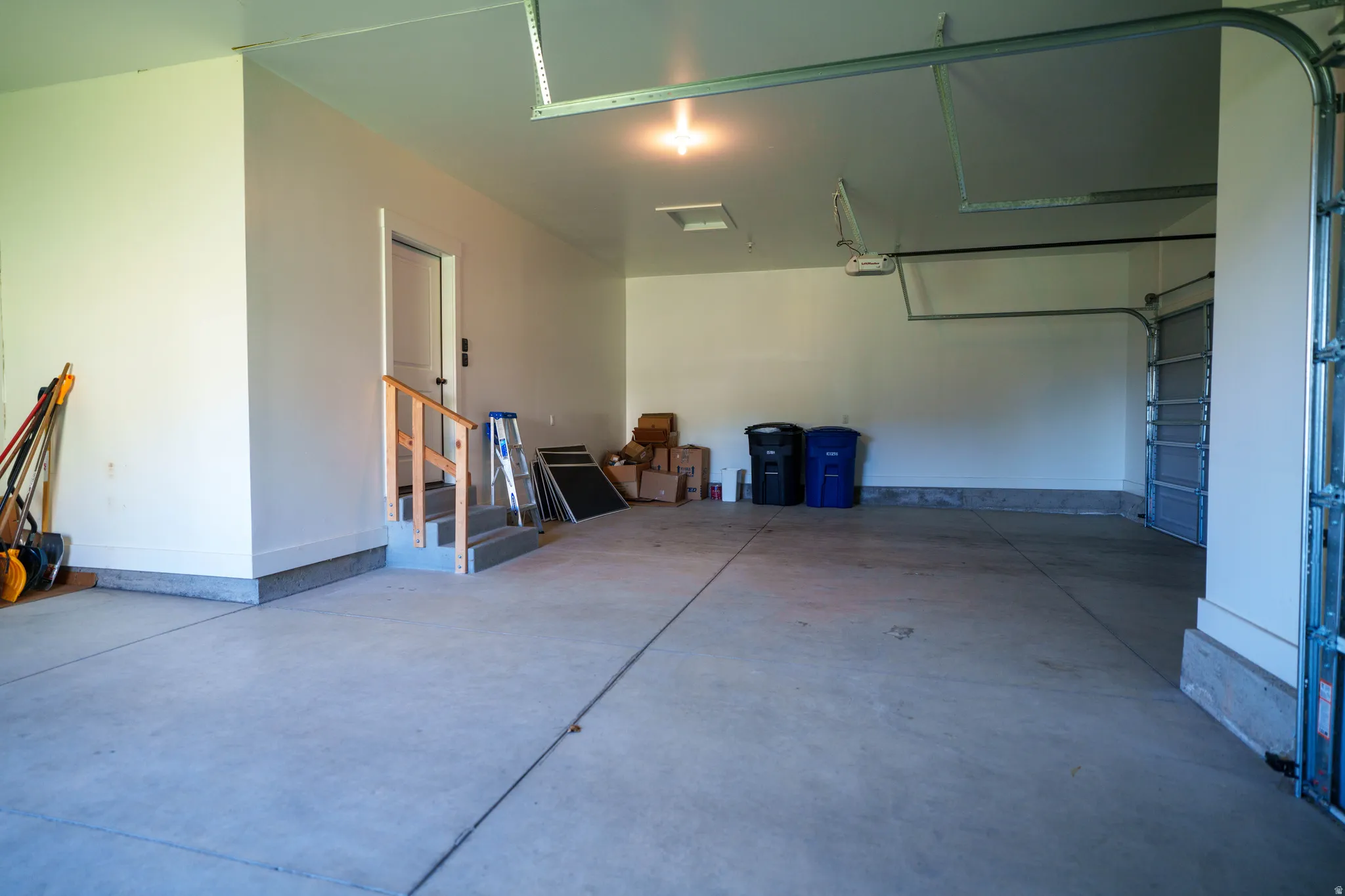 Spacious two-car garage with a concrete floor, bright overhead lighting, direct interior access, and an automatic garage door opener